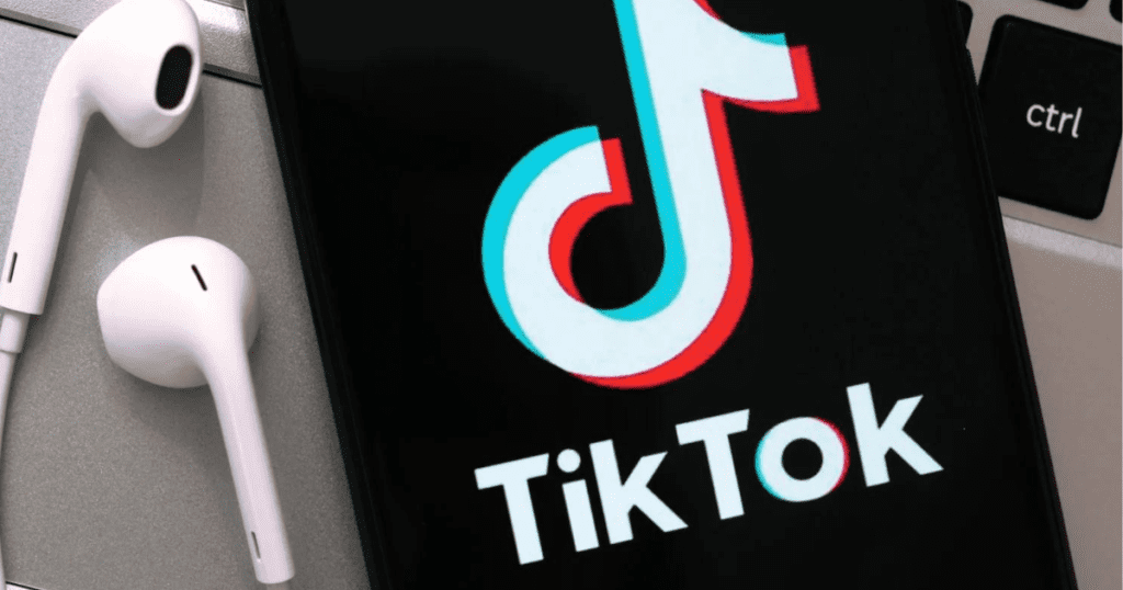 Telefonas su įjungta TikTok programėle ir ausinės pilkame fone